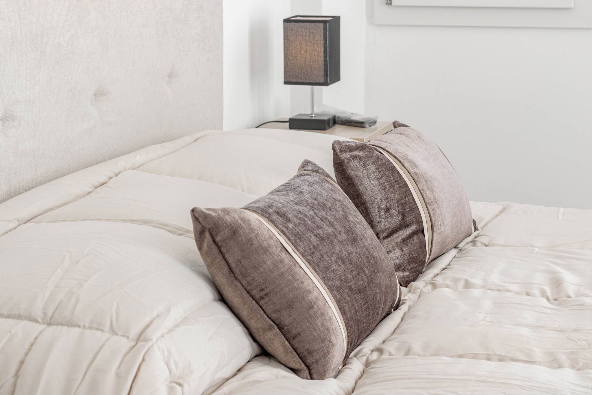 Een bed met een beige geborduurde spreideken en twee kussens met een gertextileerde stof en een contrasterende bies.