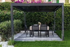 A covered outdoor seating area with a table and chairs, surrounded by a hedge and a gravel path. - VILLA MIA - Giardino-Parcheggio (Sanremo)