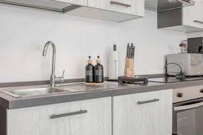 Una cocina moderna con un lavamanos de acero inoxidable, dos dispensadores negros etiquetados 'MANOS' y 'PLATOS', un porta toallas de papel y un bloque de cuchillos.