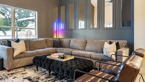 Un salon moderne avec un canapé d’angle, un pouf capitonné et une table basse sur laquelle sont posés des livres.