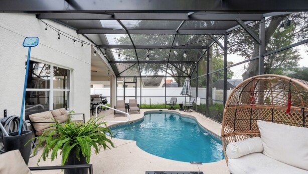 Un espace extérieur abrité avec une piscine, des chaises longues, un fauteuil en osier et un pot de fleurs.