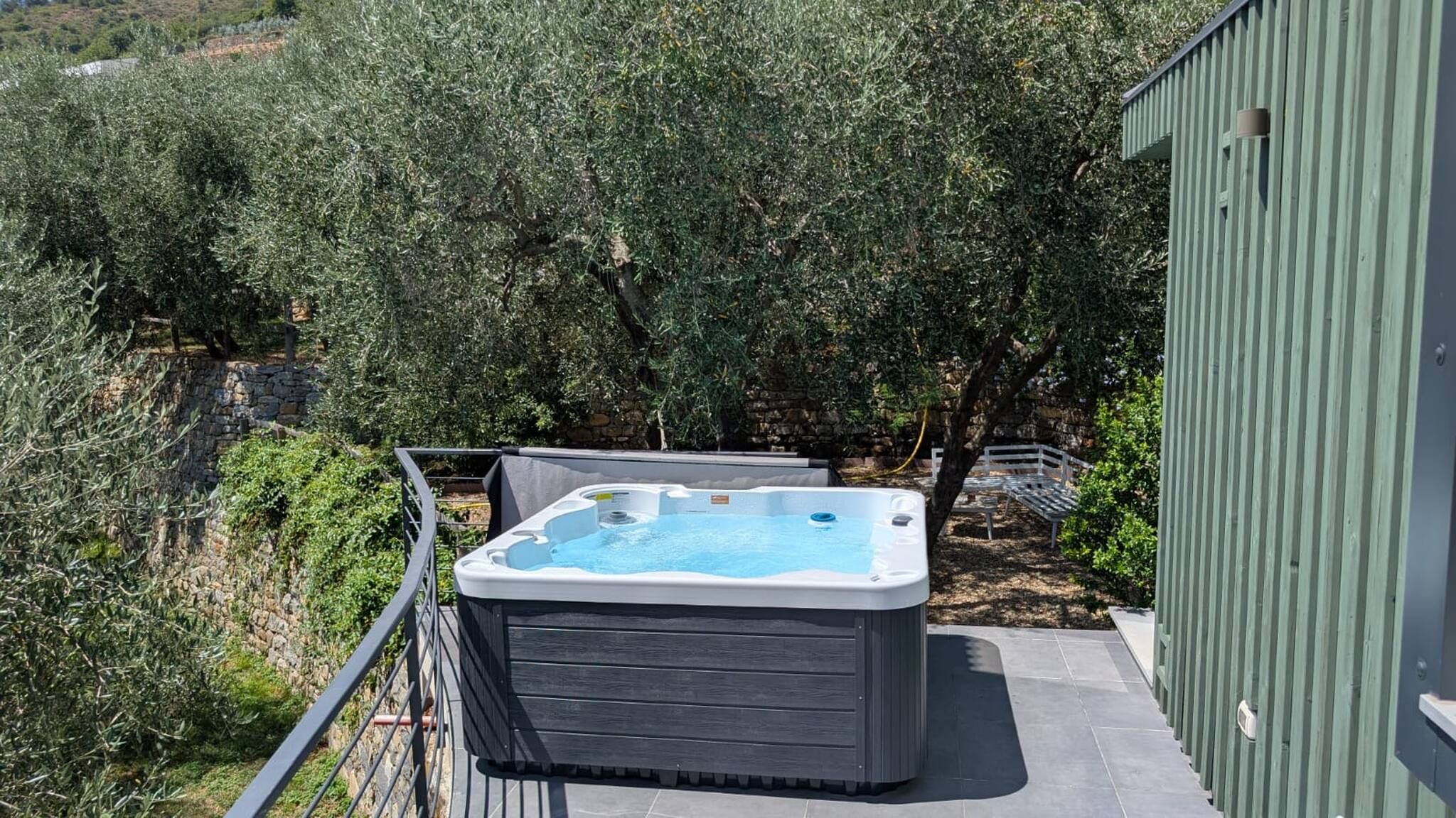 Un bain à remous sur un balcon, avec un mur en pierre et des oliviers en arrière-plan.