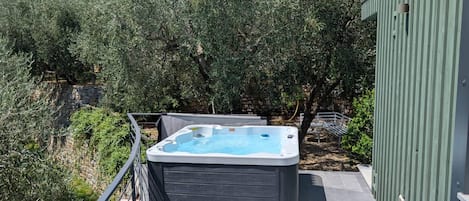 A hot tub on a balcony with a stone wall and olive trees in the background.