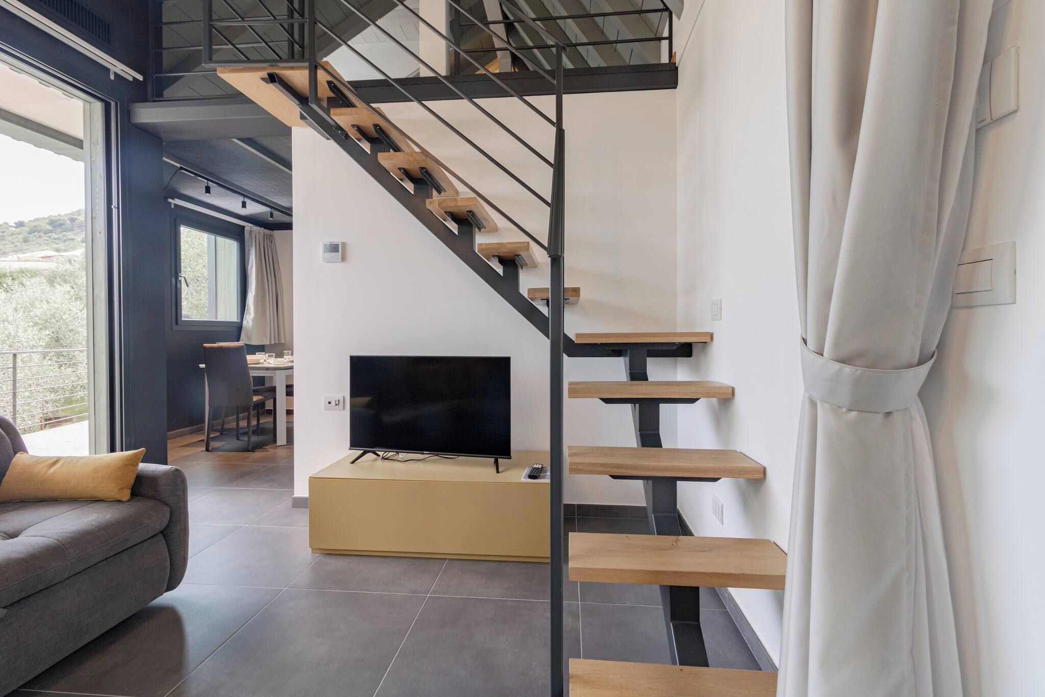 A modern interior with a staircase, a flat-screen TV, and a sofa.