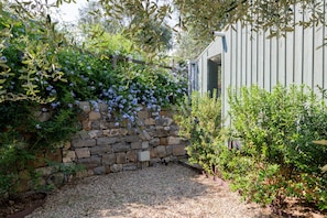 Un mur de pierres recouvert de plantes grimpantes, un chemin de gravier et une clôture en bois.