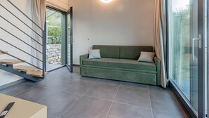 A modern living room with a green sofa, a remote control on a table, a staircase, and a glass door leading outside. - TAGGIASCA (Taggia)