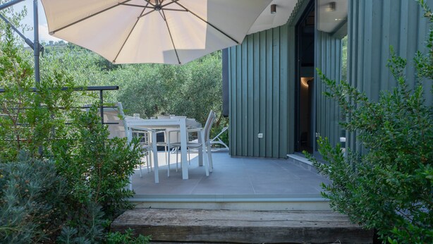 An outdoor patio with a table and chairs, a large umbrella, and a wooden deck leading to a building. - TAGGIASCA (Taggia)