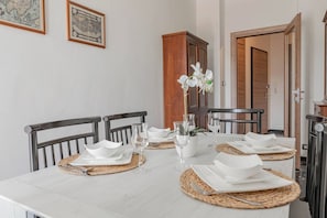 Een eettafel is gedekt met witte borden, kommen en bestek, omringd door stoelen met zwarte metalen frames.