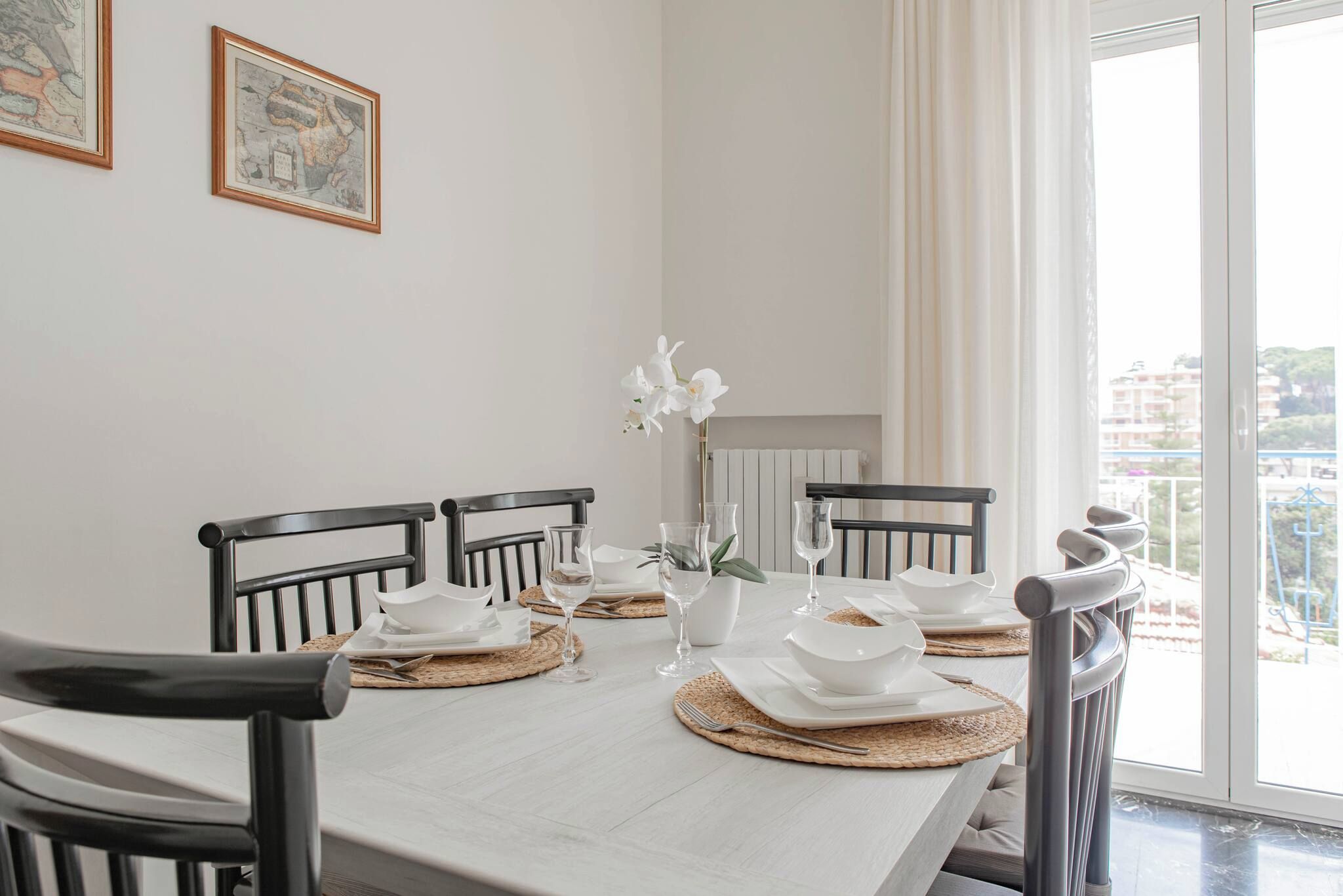 A dining table set with white plates, bowls, and wine glasses, surrounded by black chairs.