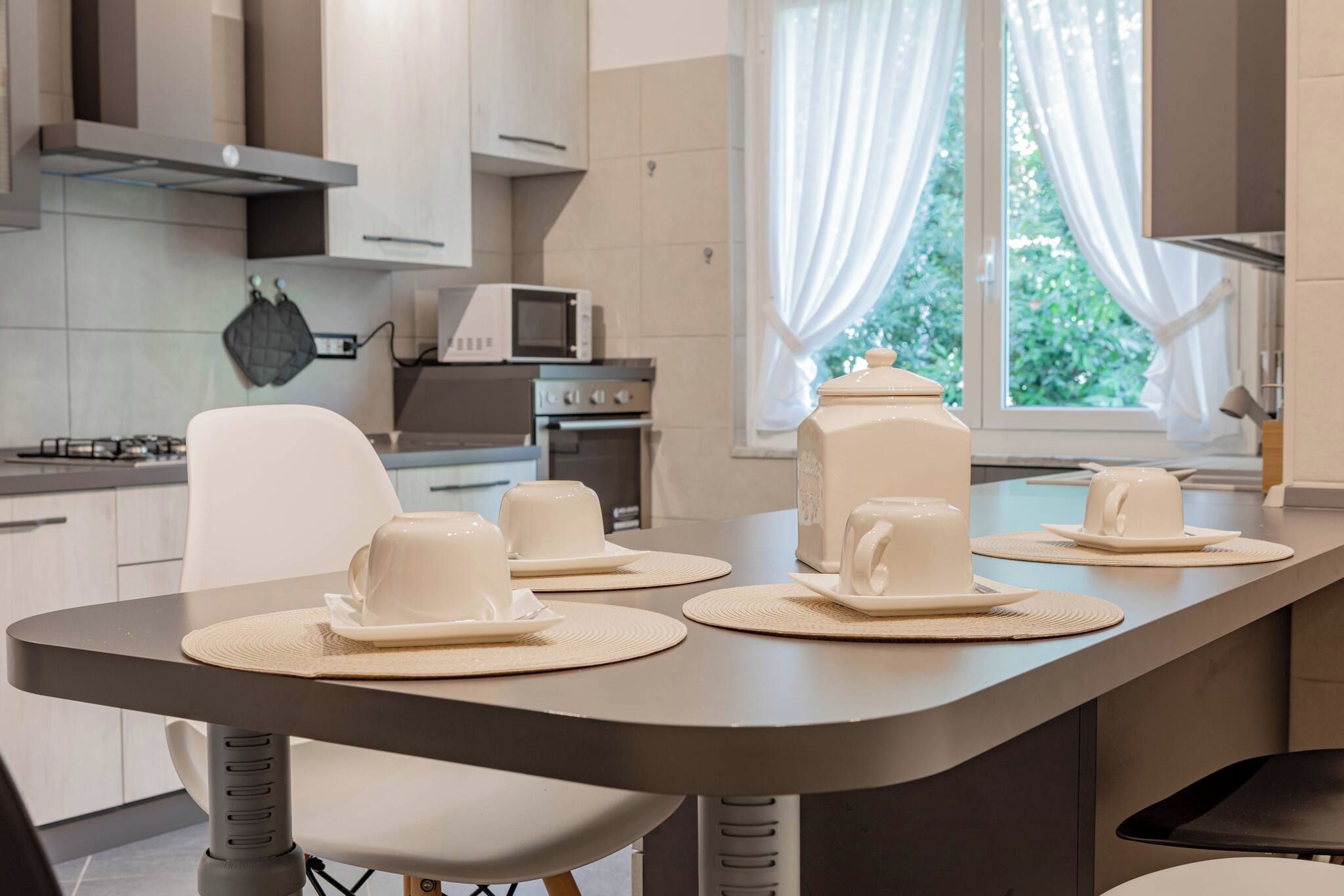 Una cucina moderna con zona pranzo, dotata di forno a microonde, piano cottura e un'ampia finestra con tende.