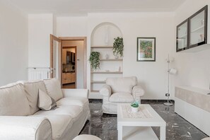 A modern living room with a sofa, armchair, and coffee table. There is a kitchen visible through an open door. - CASA DEL SOLE - Parcheggio - Vista mare (Sanremo)