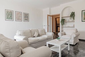 A living room with a beige sofa, a matching armchair, and a coffee table. There are three framed artworks on the wall. - CASA DEL SOLE - Parcheggio - Vista mare (Sanremo)