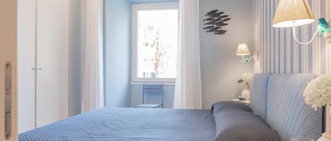 Een slaapkamer met een bed, nachtkastje, lamp, raam met gordijnen en een muur met een decoratieve muurschildering van vissen.