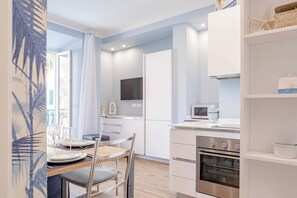 A modern kitchen with a built-in oven, a dining area with a table and chairs, and a TV mounted on the wall. - CASA CAMILLA - Centro - Sanremo (Sanremo)