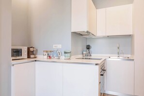 A modern kitchen with white cabinetry, a built-in microwave, a kettle, and a coffee maker. - CASA CAMILLA - Centro - Sanremo (Sanremo)