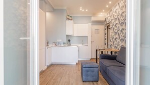 Eine moderne Küche mit weißen Schränken, einer zentralen Kochinsel und einem Essbereich mit grauem Sofa und Hocker.