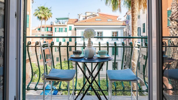 Ein Balkon mit Tisch für zwei Personen, Stühlen und einer Blumenvase.