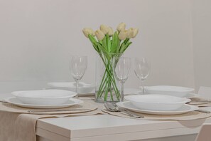 A table set with white plates, clear wine glasses, and a vase with white tulips.