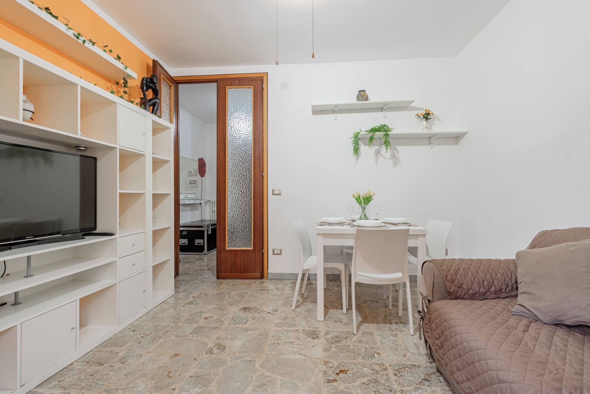 Un ambiente compatto con televisione, arredi bianchi, una zona pranzo e un angolo salotto accogliente.