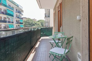 A balcony with a table and chairs, a view of buildings, and a green fence.