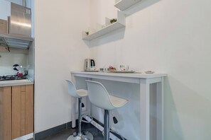 Une cuisine compacte équipée d’une cuisinière à gaz, de deux tabourets de bar blancs, d’un plan de travail blanc et d’une hotte en acier inoxydable.