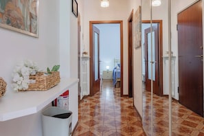 A hallway with a patterned floor, a white counter with a basket of flowers, and a door leading to another room. - CATTY'S HOUSE - Mare - Parcheggio (Santo Stefano al Mare)