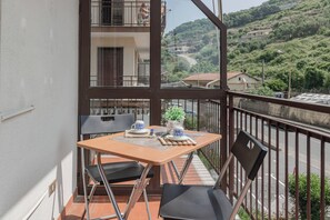 A balcony with a table set for two, chairs, and a view of a hilly landscape. - CATTY'S HOUSE - Mare - Parcheggio (Santo Stefano al Mare)
