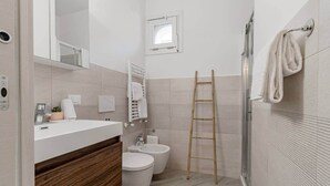 Un bagno moderno con un mobile bagno in legno, due servizi igienici, una doccia e un porta asciugamani.