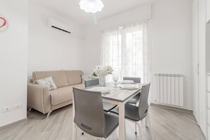 A modern dining area with a table set for two, a sofa, and a radiator. - CASA ALICE - Monolocale - Sanremo (Sanremo)