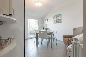 A modern kitchen with white cabinets, a dining area with a table and chairs, and a view of the outdoors through a large window. - ELENA HOUSE - Vista - Porto (Sanremo)