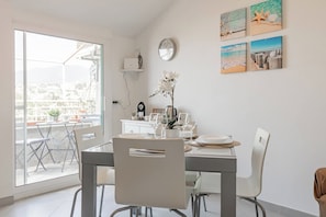 Een eetruimte met een tafel gedekt voor vier personen, stoelen, een koffieapparaat en een klok aan de muur.