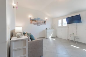 Een moderne woonkamer met een bank, bijzettafeltje en een kast. Er zijn drie aan de muur bevestigde fotolijsten en een potplant.