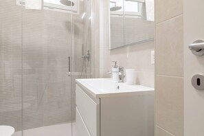 A modern bathroom with a glass shower enclosure, a white sink with a mirror, and a toilet.