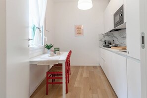 A compact kitchen with a dining area, a window with curtains, a potted plant, and a microwave. - CASA GIULIETTA - Sanremo (Sanremo)