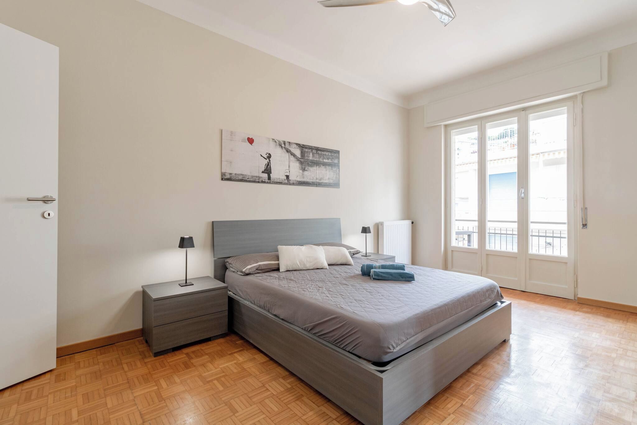 A bedroom with a bed, nightstands, a painting, and a window with a view.