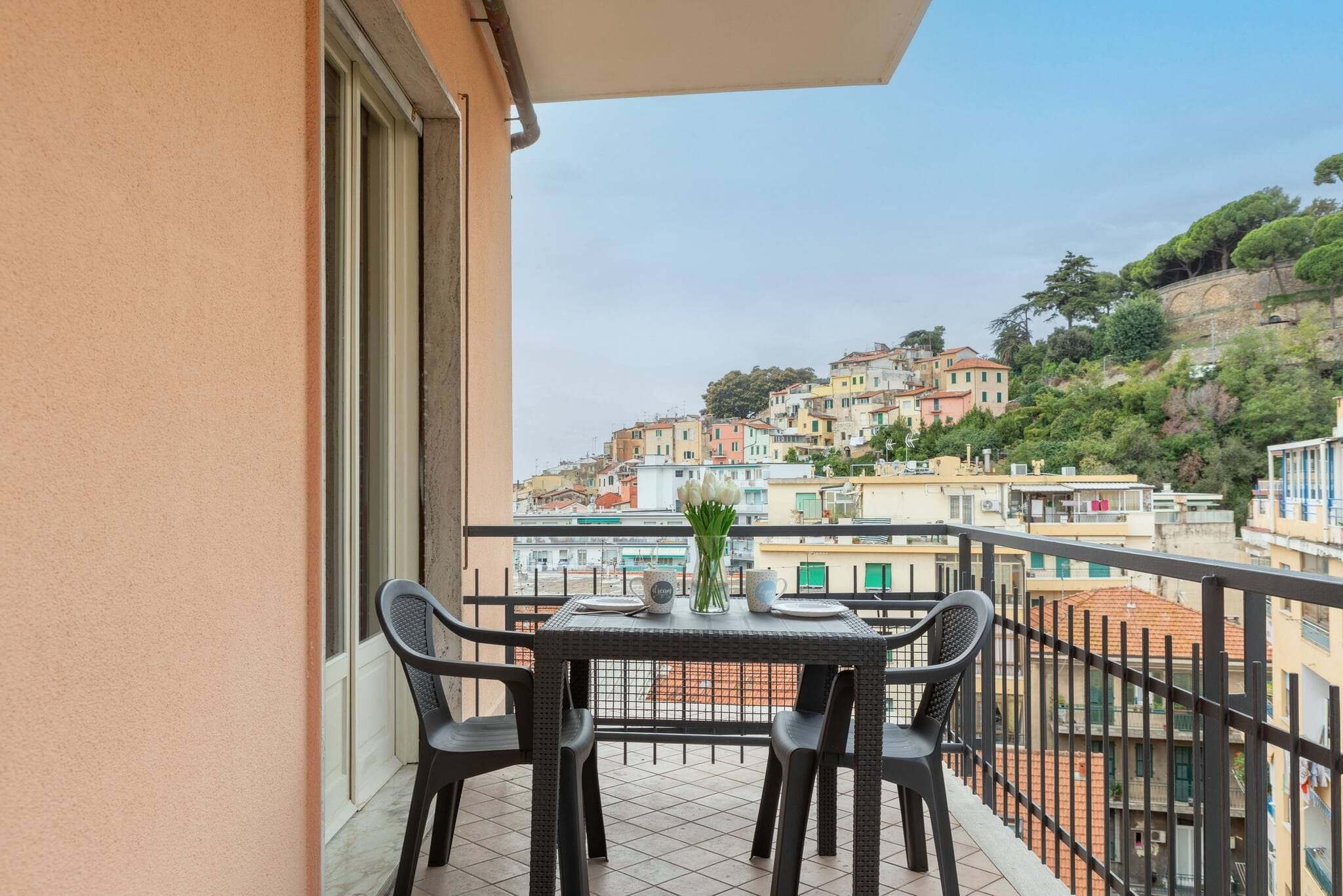 A balcony with a table and chairs, overlooking a hillside with colorful buildings.