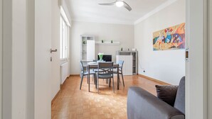 Ein modernes Wohnzimmer mit grauem Sofa, einem Essbereich mit Tisch und Stühlen, einem Deckenventilator und einer Küchenzeile mit Schränken und einem Fernseher.