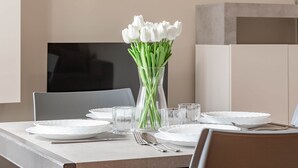 Ein Esstisch, gedeckt mit weißen Tellern, klaren Gläsern und einer Vase mit weißen Blumen.
