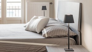 Ein ordentlich bezogenes Bett mit gestreifter Bettwäsche und einer modernen Lampe daneben.