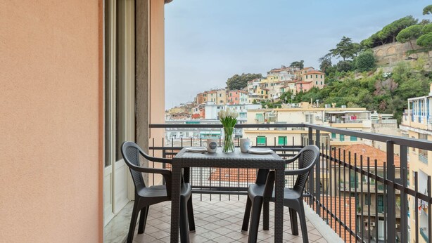 Ein Balkon mit Tisch und Stühlen, der einen Blick auf eine Hügelkuppe mit bunten Häusern bietet.