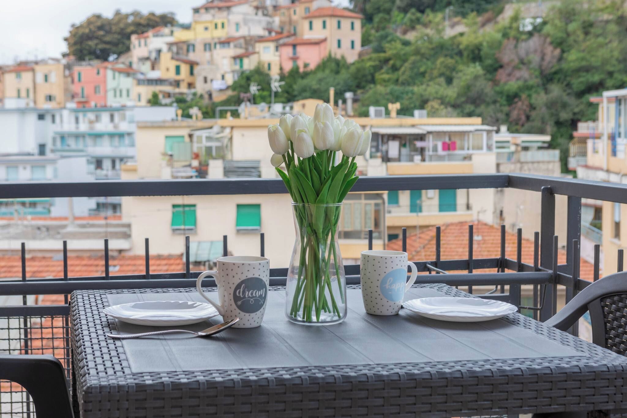 A balcony with a table set for two, a vase with white flowers, and two mugs with text.