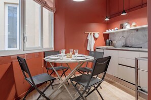 A compact kitchen with a dining table set for four, a small island with a kettle, and a window with curtains. - CENTRAL CHARM - Sanremo - Ariston (Sanremo)