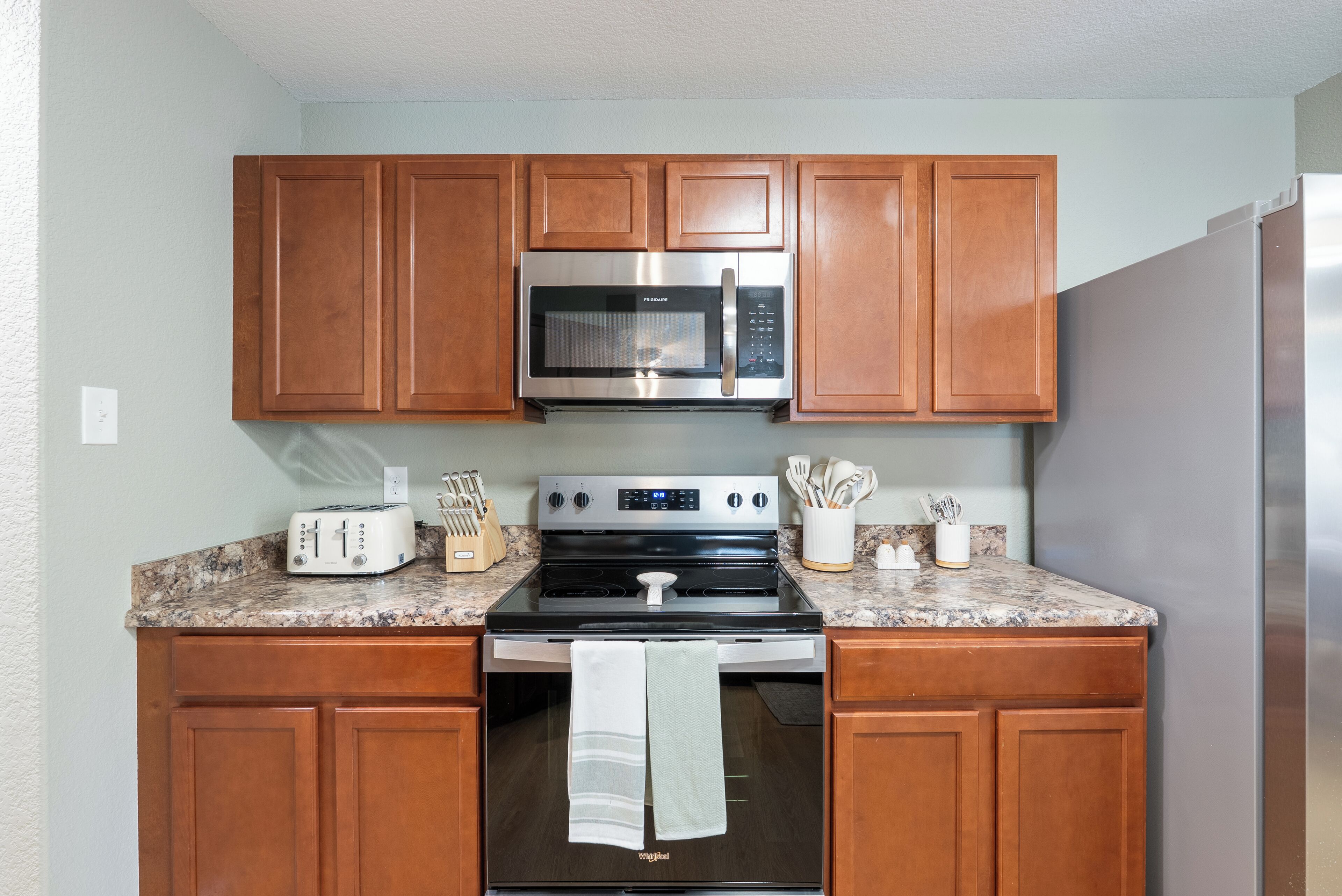 A kitchen with wooden cabinets, a stainless steel microwave, a stove, and a refrigerator.