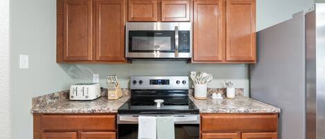 A kitchen with wooden cabinets, a stainless steel microwave, a stove, and a refrigerator.