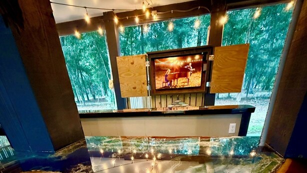 Une pièce dotée d’un grand sol au design réfléchissant, d’un coin bar avec un téléviseur et d’une vue sur les arbres à travers de grandes fenêtres.