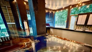 Une pièce dotée d’un grand élément décoratif aquatique au centre, de poutres en bois et offrant une vue sur les arbres à travers les fenêtres.