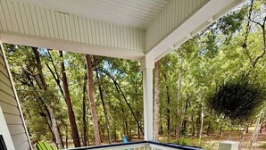 Une véranda couverte, avec des fauteuils Adirondack verts et une petite table, le tout entouré d’une balustrade blanche et d’arbres.