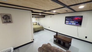 Une chambre moderne avec un lit, un téléviseur fixé au mur, un banc en bois et un tableau encadré accroché au mur.