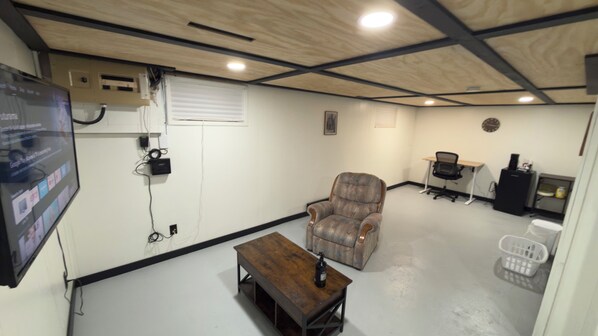 A room with a wooden ceiling, a television mounted on the wall, a couch, a small table, and a desk with a chair.