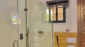 Ducha con cerramiento de vidrio, tocador de madera y lavamanos blanco.